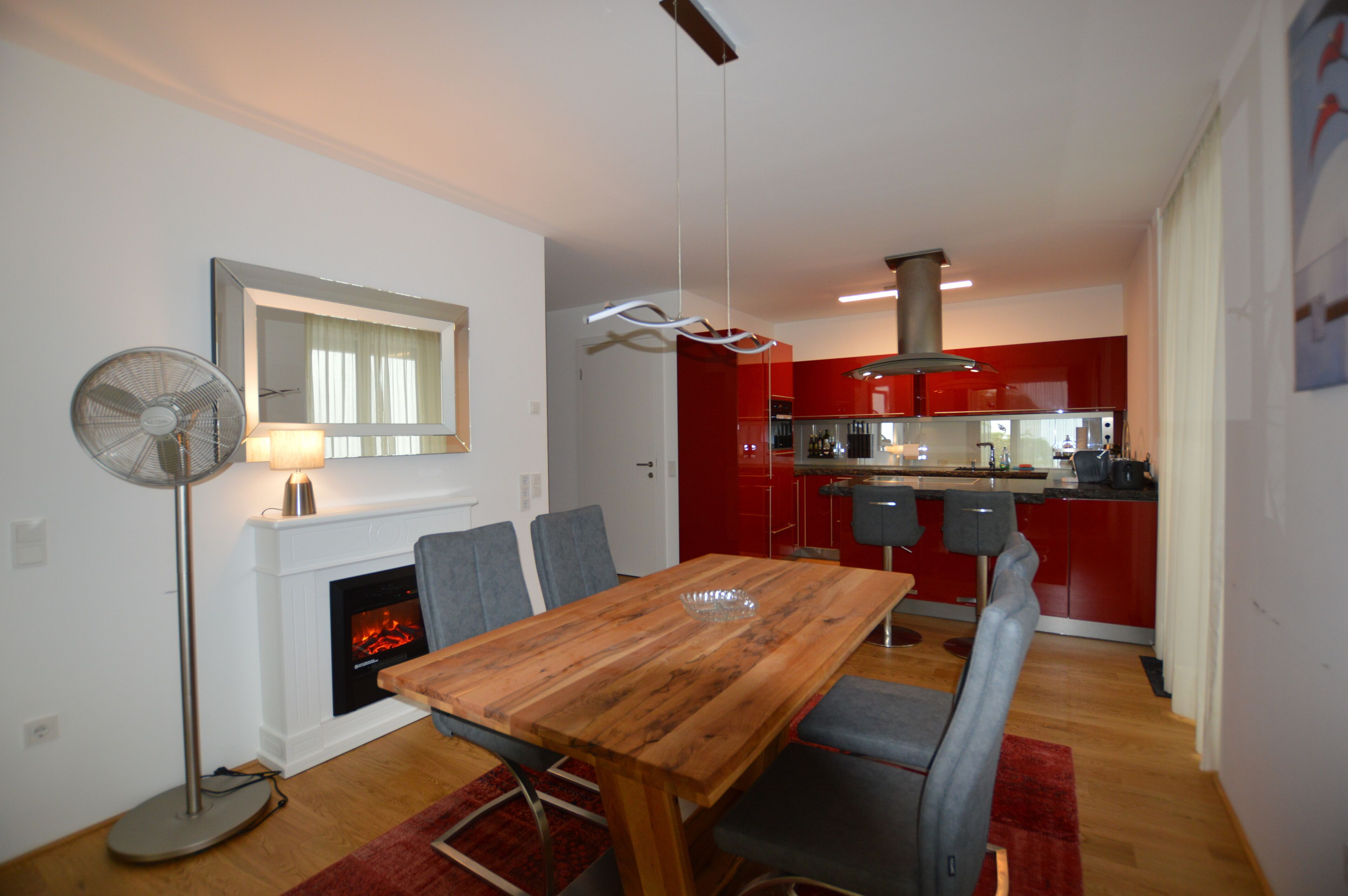 Un coin repas avec une table et des chaises en bois, une cheminée, et une cuisine moderne en arrière-plan.