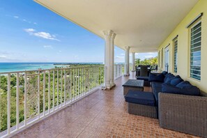 A balcony with a view of the ocean, white columns, and outdoor furniture. - Tropical Retreat with Ocean View Oasis + Pool (Luquillo)