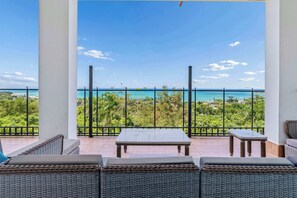 A balcony with wicker furniture, a table, and a view of the ocean. - Tropical Retreat with Ocean View Oasis + Pool (Luquillo)