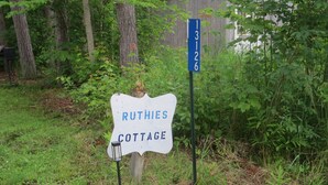 Une enseigne en bois rustique portant l’inscription « Ruthies Cottage » et une autre enseigne bleue avec les chiffres « 3126 », indiquant une adresse.