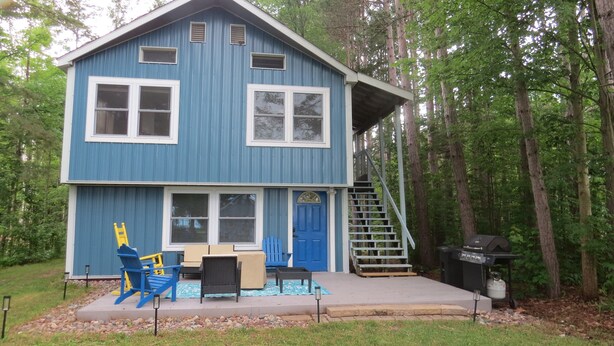 Une cabane bleue à deux étages, dotée d’un porche à l’avant, d’un escalier et de meubles pour s’asseoir à l’extérieur.