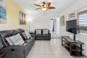 A living room with a sofa, TV, and ceiling fan.