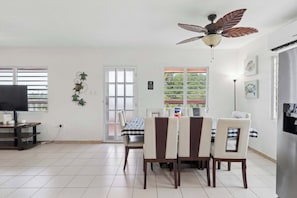 A dining area with a ceiling fan, a TV, and a refrigerator.