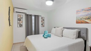 A bedroom with a bed, air conditioning unit, curtains, a painting, and a tiled floor. - Tropical Oasis Retreat & Infiniti Pool (Luquillo)