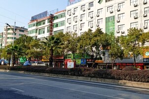 Un edificio de varios pisos con unidades de aire acondicionado, una calle al frente y varios comercios con letreros.