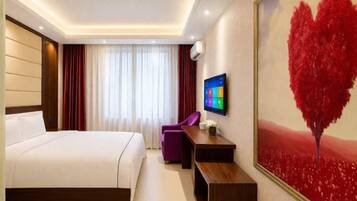 Habitación de hotel con cama, escritorio, silla, televisor y un cuadro grande con forma de corazón en la pared.