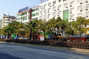 Un edificio a più piani con file di negozi al piano terra, cielo sereno e strada in primo piano.