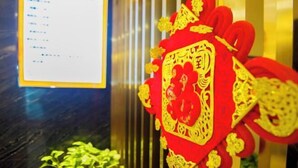 A red and gold decorative item with intricate designs, possibly a traditional ornament, hanging in a room with a dark floor and a glass partition. - Fubang Hotel (Yichun)