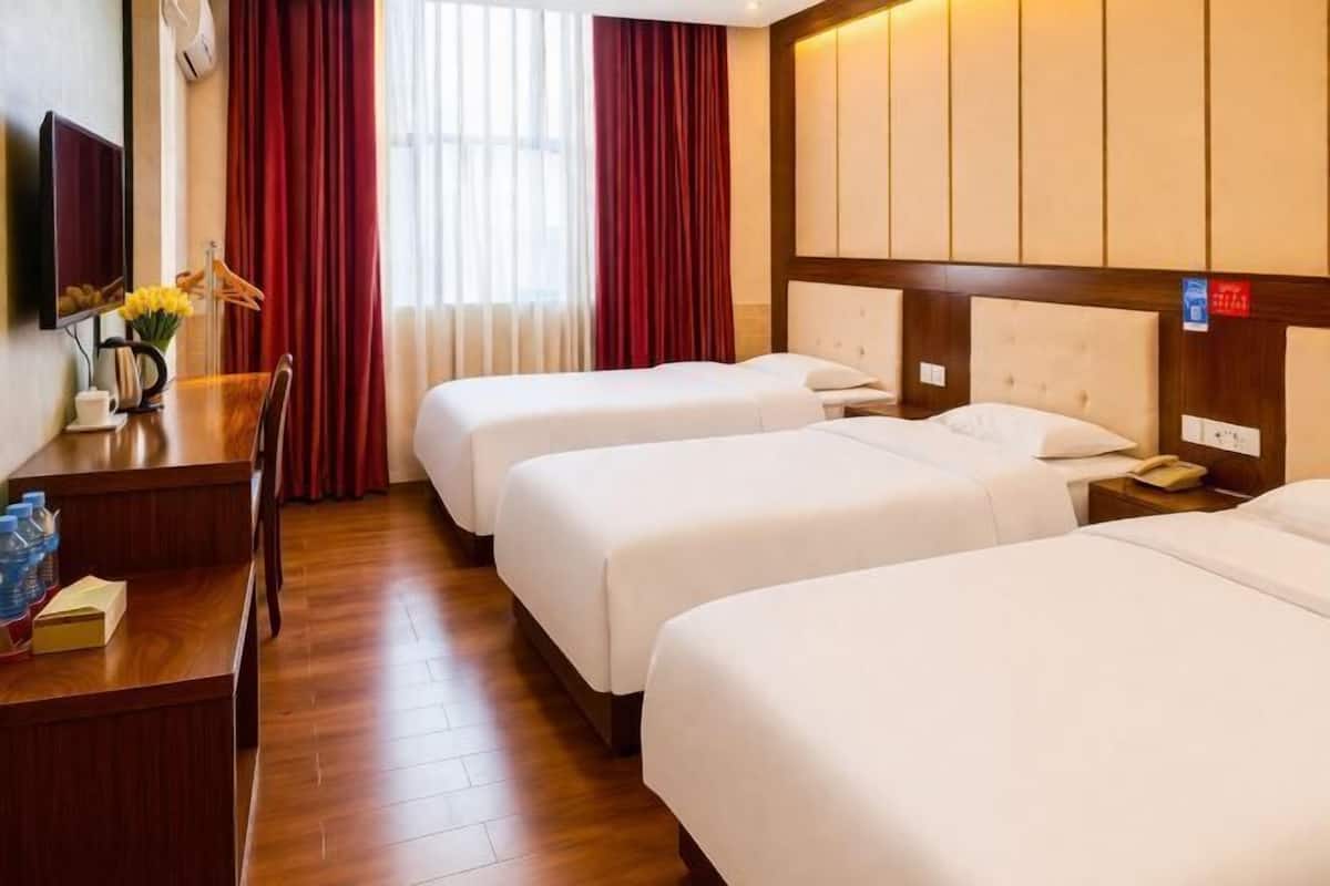 A hotel room with two beds, a desk with a chair, a TV, and a window with red curtains.