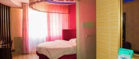 A bedroom with a bed, a desk, and a window with curtains.
