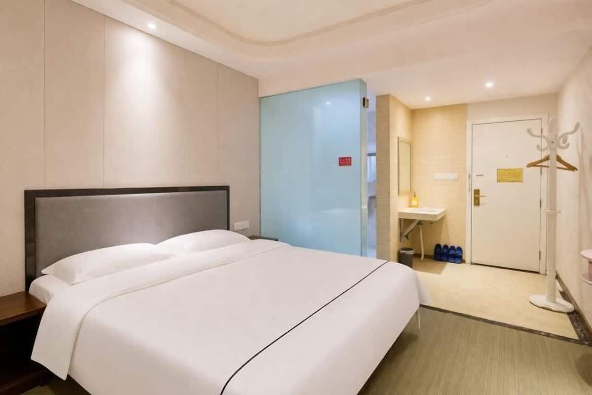 A hotel room with a large bed, a bedside table, a wardrobe, a bathroom with a sink, and a coat rack.