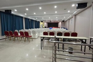 Un salón de conferencias con filas de sillas, mesas y una zona de escenario.