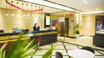 A hotel reception area with a reception desk, a receptionist, and a seating area with a table and chairs.