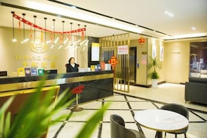 Zona de recepción de un hotel, con mostrador, recepcionista y un área de estar con mesa y sillas.