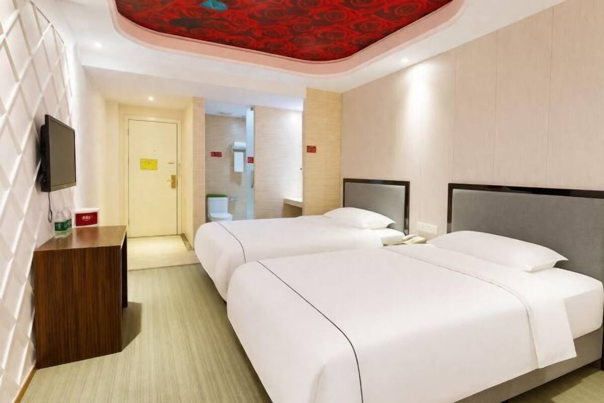 A hotel room with two beds, a wooden desk, a television, and a red patterned ceiling.