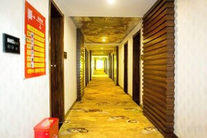 Un pasillo de hotel con alfombra estampada, puertas de madera y un cartel informativo rojo en la pared izquierda.