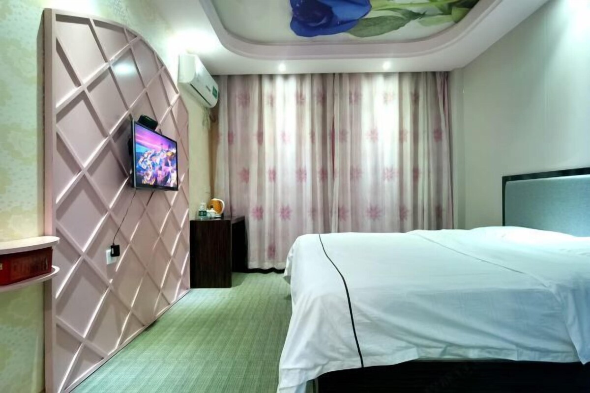 A hotel room with a bed, a TV mounted on a wall, a small table, and a curtain with a floral pattern.