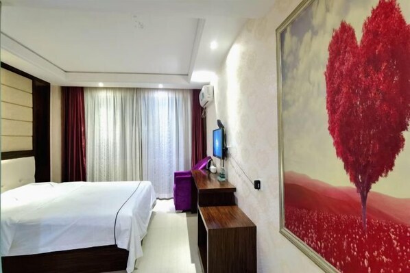 A hotel room with a bed, a desk, a TV, and a painting of a red tree.