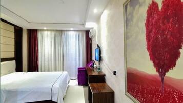 A hotel room with a bed, a desk, a TV, and a painting of a red tree.