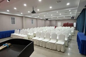 Una sala conferenze con file di sedie bianche, un palco e un tavolo blu sulla destra.