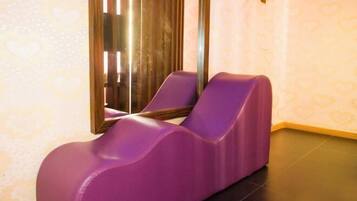 A massage chair in a room with patterned wallpaper and a large mirror.