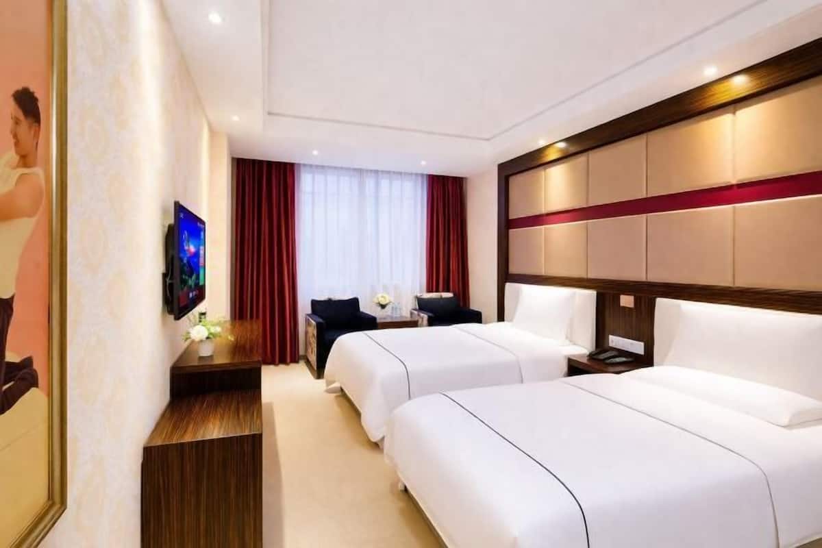 A hotel room with two beds, a TV, a desk, and a window with curtains.