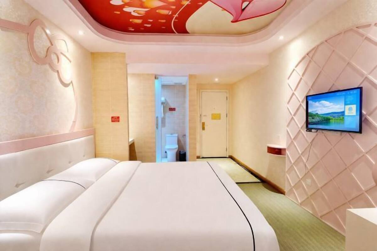 A hotel room with a large bed, a television mounted on the wall, and a door leading to a bathroom.