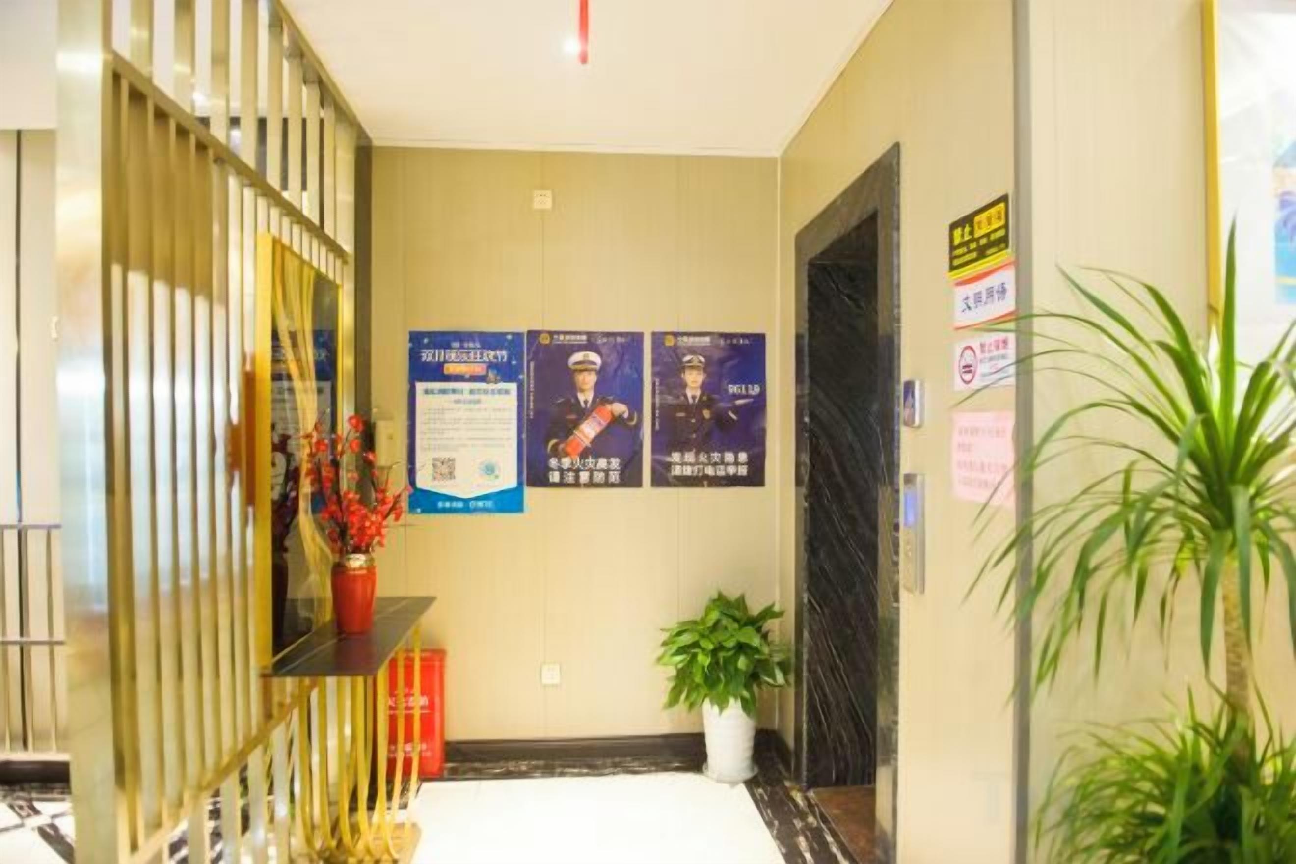 Um saguão de hotel com uma recepção, um vaso de plantas e cartazes informativos na parede.