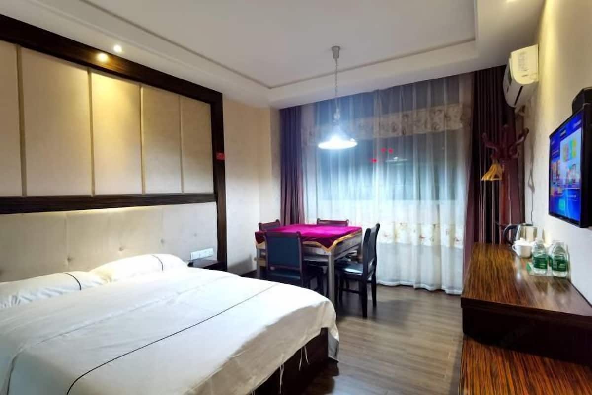 A hotel room with a large bed, a dining table with chairs, a TV, and a wooden side table with bottles.