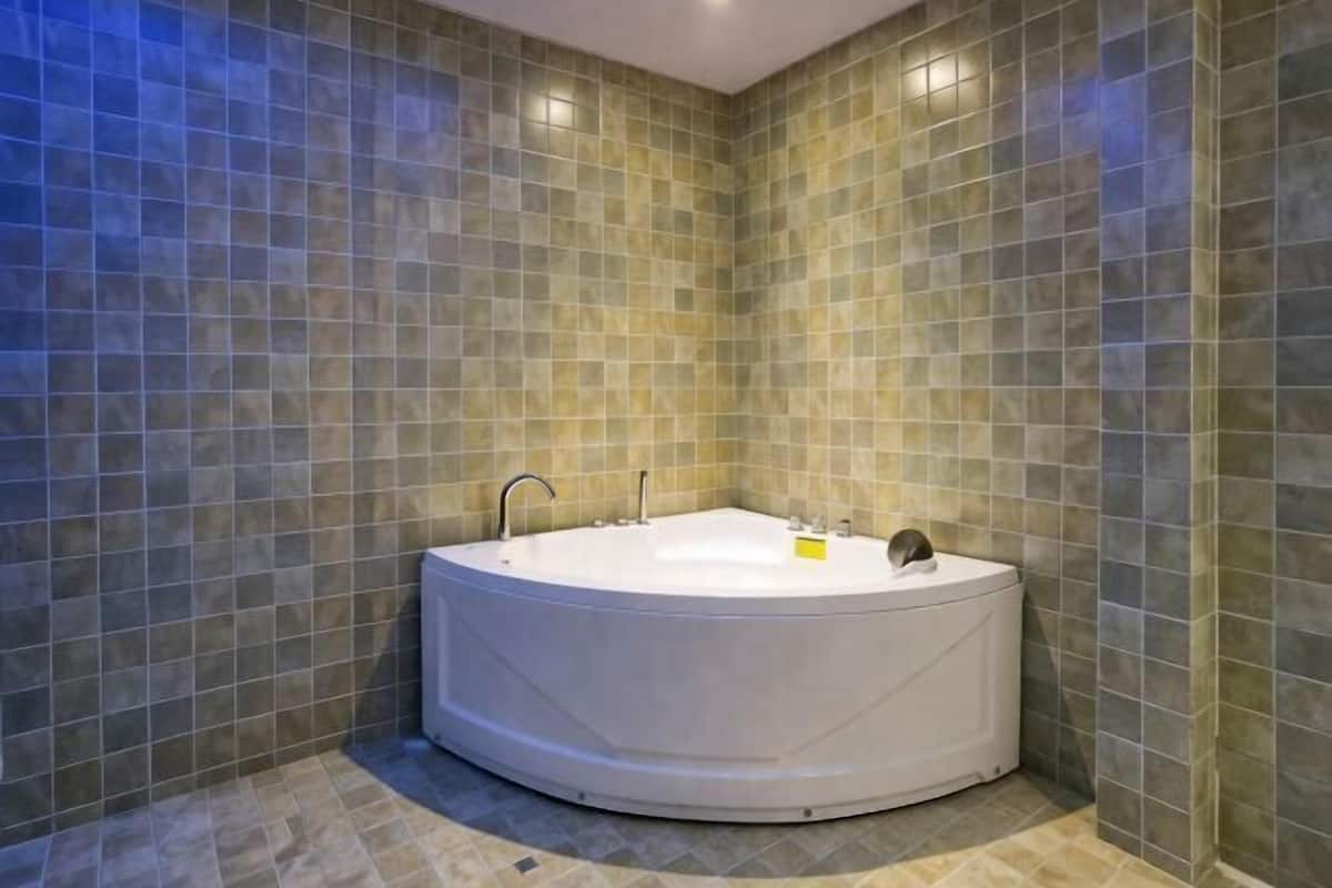 A circular jacuzzi in a corner with a tiled wall and floor.