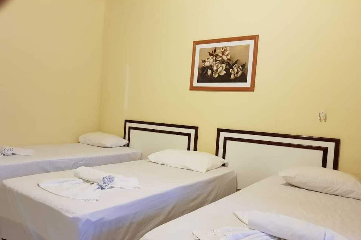 Ett hotellrum med tre enkelsängar, alla med ett vitt överkast och kuddar. På väggen ovanför sängarna hänger en inramad tavla.