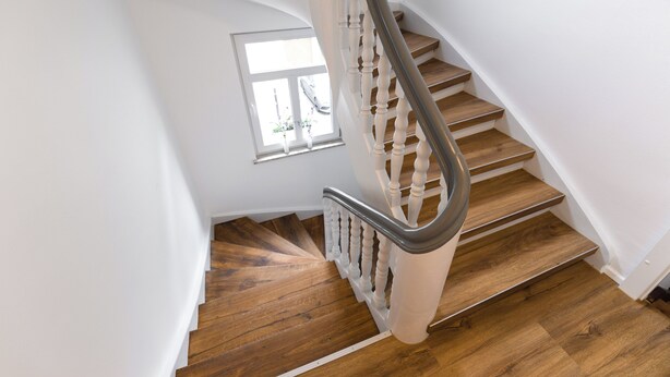 A wooden staircase with a metal handrail, white walls, and a window with a plant. - Gasthaus zur Traube (Uffenheim)