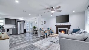Ein modernes Wohnzimmer mit Kamin, Deckenventilator und einem an der Wand befestigten Fernseher.