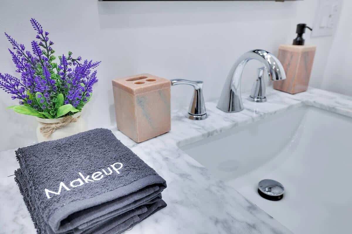 Une salle de bain avec un lavabo en marbre, deux robinets, un distributeur de savon et une serviette étiquetée « Maquillage ».