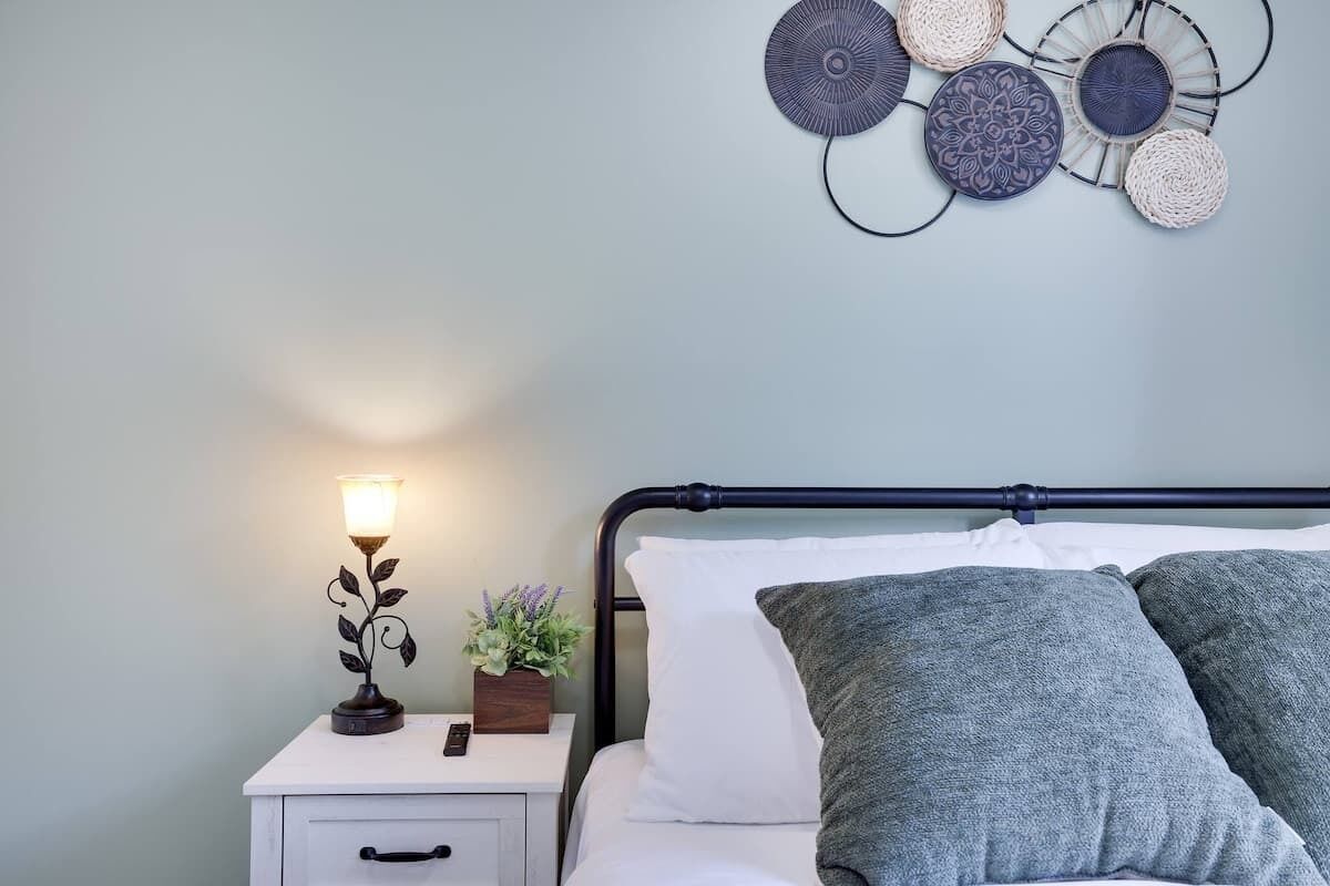 A neatly made bed with grey pillows, a bedside lamp, and a small plant on a white nightstand.