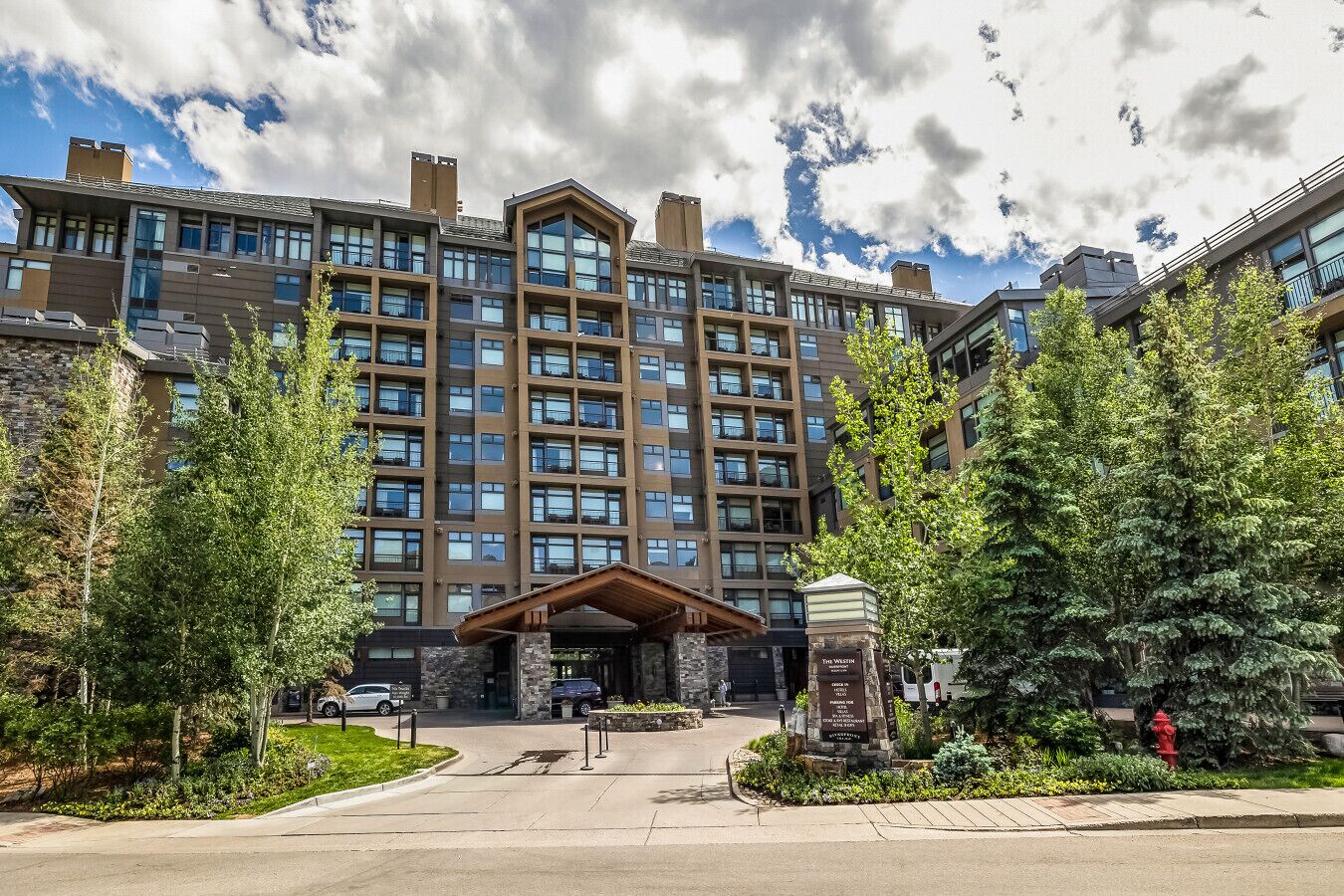 A multi-story hotel with a central entrance, surrounded by trees and a parking area.