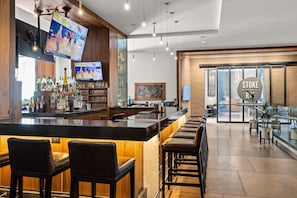 A modern bar area with a long counter, multiple stools, and a television displaying sports. - Riverfront Resort: pool, spa, athletic center (Avon)