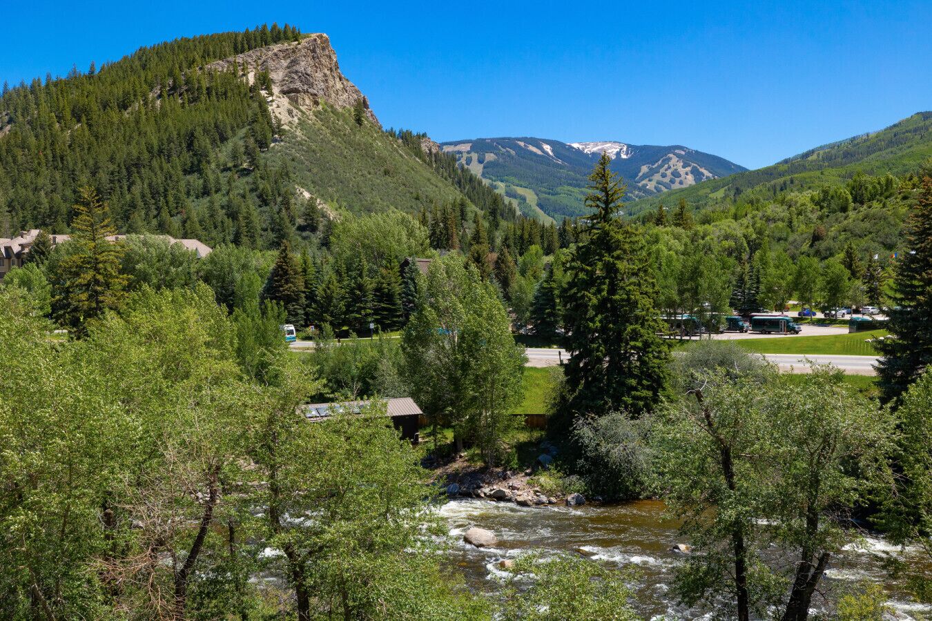 A mountainous landscape with a river, trees, and a small building.