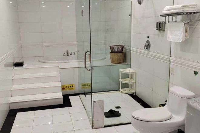 A bathroom with a glass-enclosed shower, a white bathtub, a toilet, and a small shelf with towels.