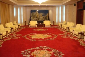 Une salle de conférence avec un tapis rouge, des chaises blanches et un grand tableau accroché au mur.