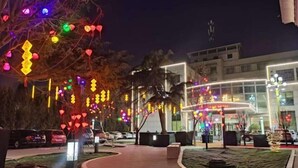Een hotelentree met een gebogen pad, bomen versierd met kleurrijke verlichting, en een gebouw met verlichte borden.