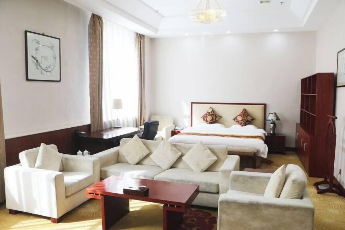 A hotel room with a bed, two sofas, a desk, a chandelier, and a bookshelf.