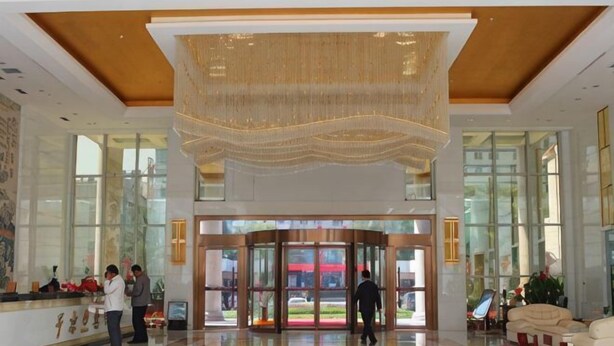 Een hotel lobby met een receptiebalie, een grote kroonluchter, een draaideur en een zithoek met een bank.