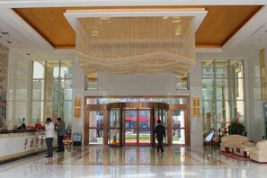 A hotel lobby with a reception desk, a large chandelier, a revolving door, and a seating area with a sofa. - Pingliang Hotel (Pingliang)