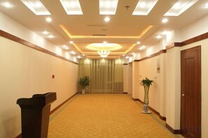 A hotel hallway with carpeted flooring, a wooden door on the right, and a plant in the center. - Pingliang Hotel (Pingliang)