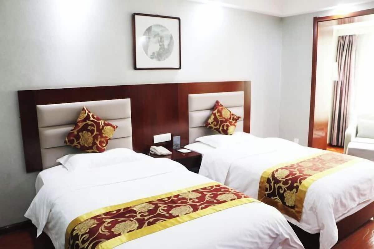 A hotel room with two beds, a wooden headboard, a nightstand, a framed picture on the wall, and a window with curtains.