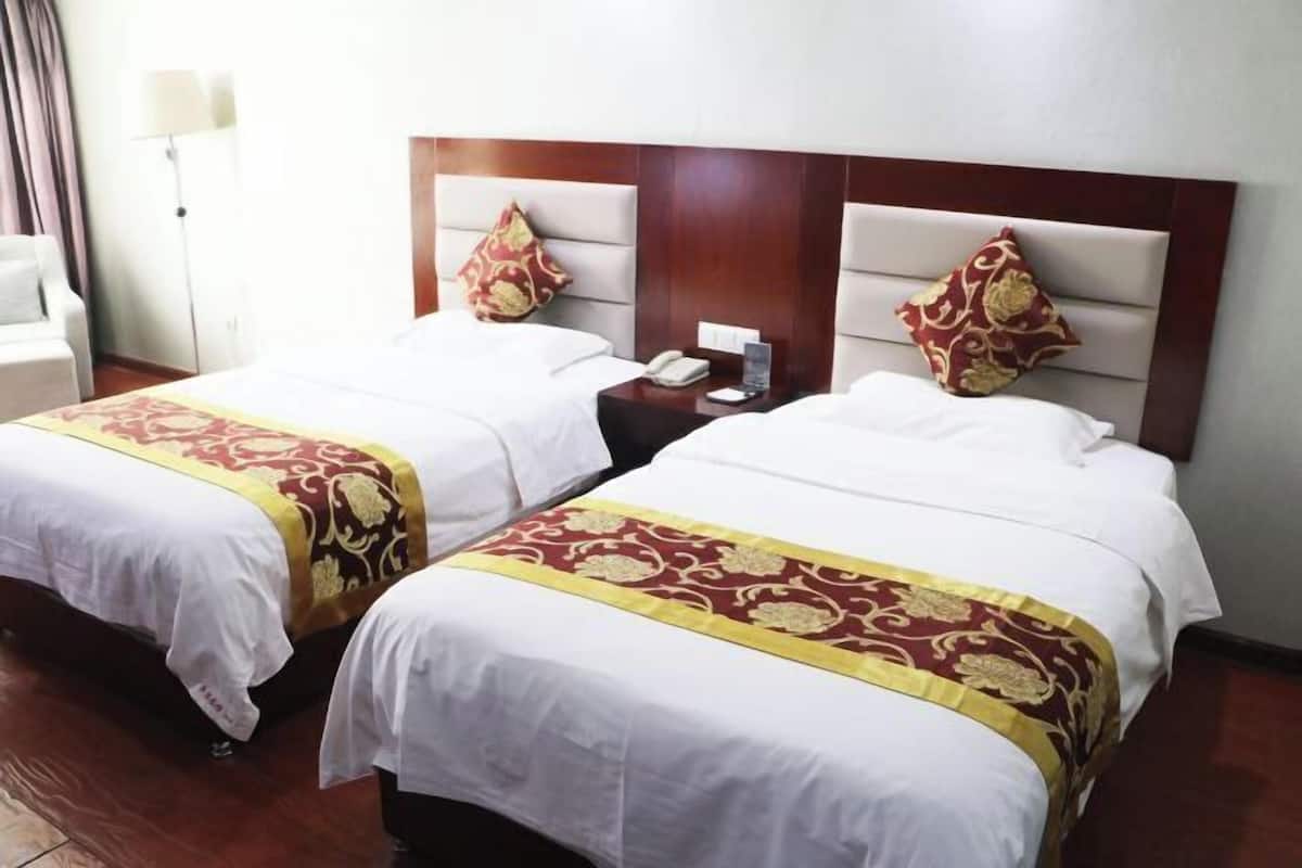 Two adjacent hotel beds with matching headboards, a bedside table with a phone, and a lamp.