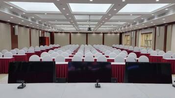 Un salón de conferencias con filas de sillas blancas, una mesa larga con mantel rojo y un techo con tragaluces.