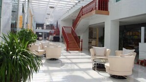 Een ruime lobby met een hoge plafond, een centrale trap en zithoeken.