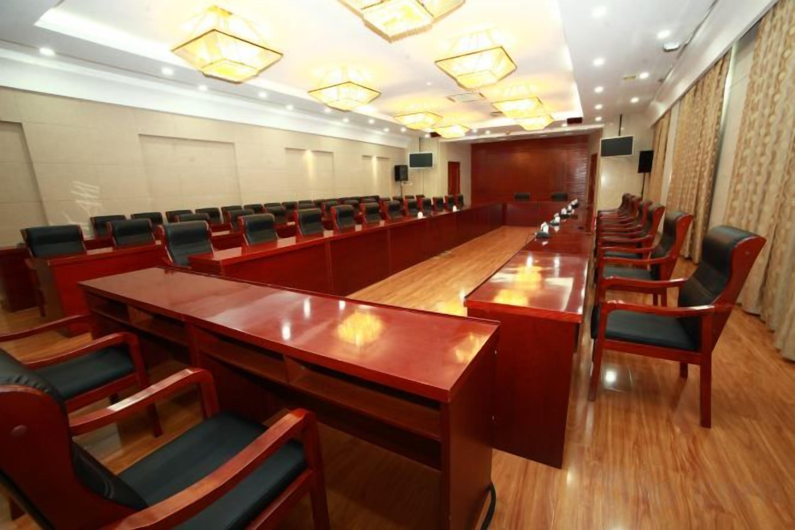 Un salón de conferencias con una mesa larga y sillas, equipado con un proyector y una pantalla.